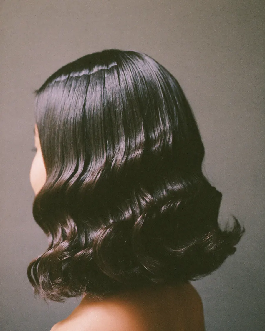 Shoulder-length black hair in loose soft-perm waves.